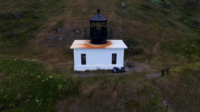 Aerial view of the historic Punta Gorda Lighthouse on the Lost Coast Trail with its white structure and black lantern room set against a grassy hillside in Whitethorn, California, United States.