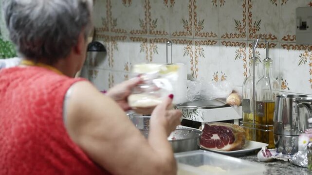  Mujer mayor rebozando alb&oacute;ndigas caseras en un bol de pan rallado. Abuela mayor enrollando y rebozando alb&oacute;ndigas en pan rallado. Receta casera tradicional, aut&eacute;ntica cocina senior.