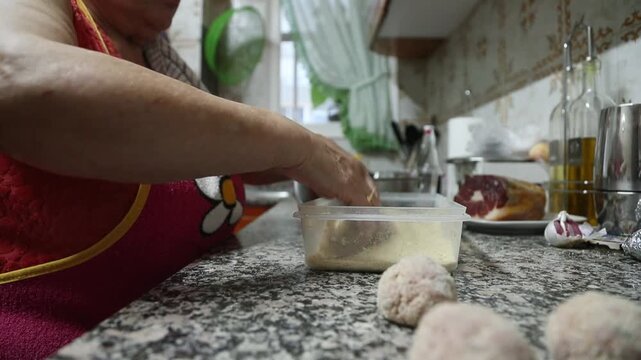  Mujer mayor rebozando alb&oacute;ndigas caseras en un bol de pan rallado. Abuela mayor enrollando y rebozando alb&oacute;ndigas en pan rallado. Receta casera tradicional, aut&eacute;ntica cocina senior.