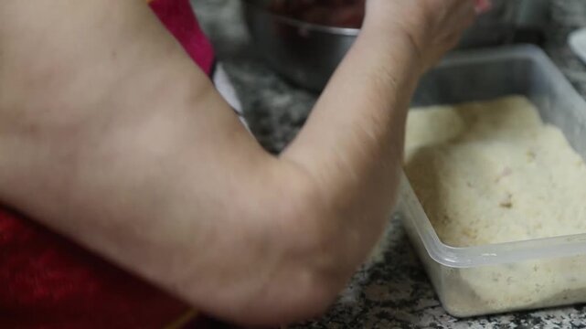  Mujer mayor rebozando alb&oacute;ndigas caseras en un bol de pan rallado. Abuela mayor enrollando y rebozando alb&oacute;ndigas en pan rallado. Receta casera tradicional, aut&eacute;ntica cocina senior.