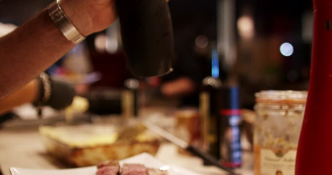 Close-up of a chef seasoning a sliced steak dish with a black pepper grinder in a kitchen