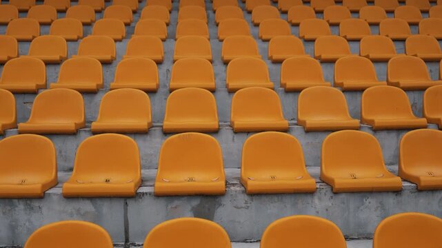 Smooth tracking shot of empty orange plastic stadium seats arranged in repeating rows. Abstract geometric pattern and sports venue background, ideal for themes of architecture, attendance, events and 