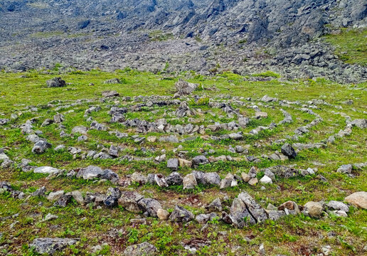 Stone labyrinth on the alpine meadow with green grass among rocks
