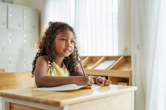 Cute young girl writing in a notebook during a lesson at school, Happy student girl studying and learning in modern classroom, Education concept, primary school student focused on writing in book
