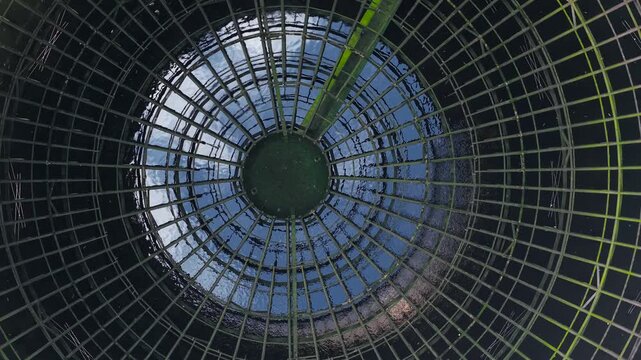 Radial metal framework inside nuclear cooling tower with circular geometry and reflective water surface. Industrial energy infrastructure concept linked to power generation and global energy crisis