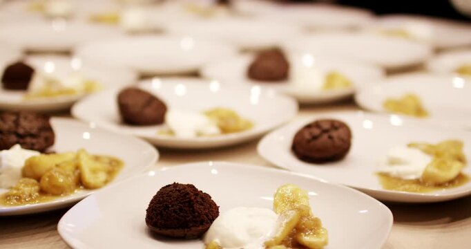 Rows of white plates containing freshly baked chocolate muffins and sliced banana dessert on a counter