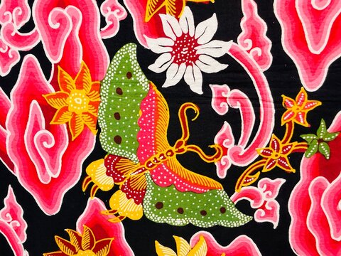 A beautiful Indonesian batik fabric featuring butterfly, flower, leaf, and cloud motifs from Cirebon, dominated by red and black colors.