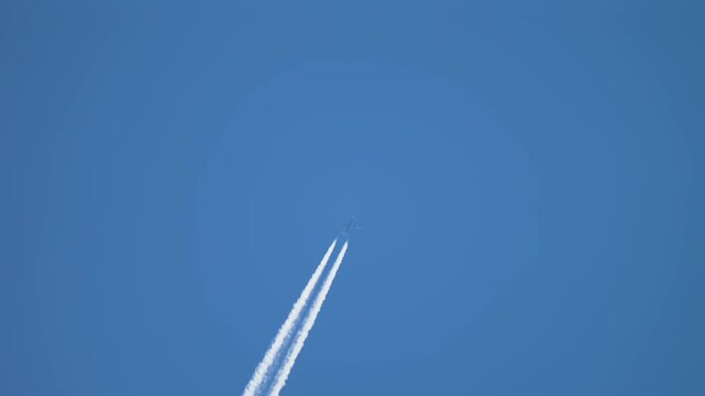 Airliner ascending with bright twin contrails cutting through clear blue sky, high altitude climb and aviation route concept. Vapor trails extending long distance emphasizing jet propulsion and
