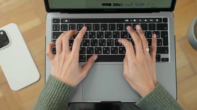 Professional woman typing on laptop keyboard, top view of female hands working on computer, remote office workspace with smartphone