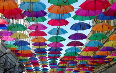 Colorful umbrellas hanging over a city street against a blue sky, creative urban decoration, summer tourism concept. © алексей орлов