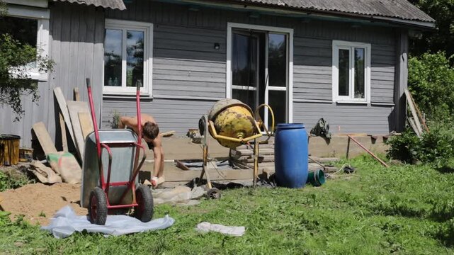 A man mixes concrete mortar for house repairs and foundation replacement, using a concrete mixer