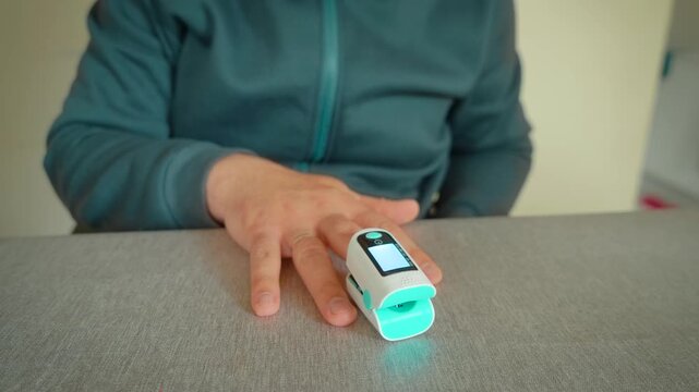 Blood oxygen monitoring with fingertip pulse oximeter device. Hands using digital oxygen saturation meter for pulse rate measurement indoors. Medical screening for coronavirus flu symptoms breathing