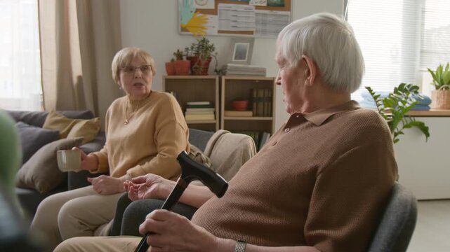Side view zoom in shot of senior man holding walking cane talking with senior woman in retirement home. For senior care services, nursing home marketing and retirement planning ads