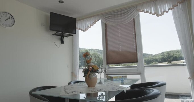 Bright indoor dining area with a glass table and a wall mounted television near a large window