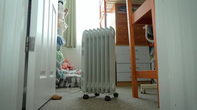Oil radiator heater warming small bedroom during winter season. Portable electric heating appliance standing near window and study desk. Home comfort, cold weather heating, and indoor temperature