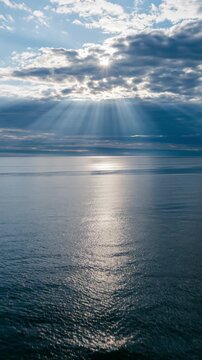Sun rays shining through dark clouds over the ocean. God rays reflecting on water surface. Dramatic seascape and weather concept