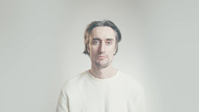 Young adult man giving slight nod of approval, calm expression, minimalist studio portrait on neutral background with soft lighting