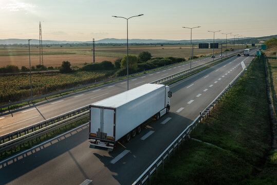White transportation truck with semi-trailer driving along highway on the sunset background. Services and Transport logistics. Modern Lorry Transport concept. Long Self-driving lorries