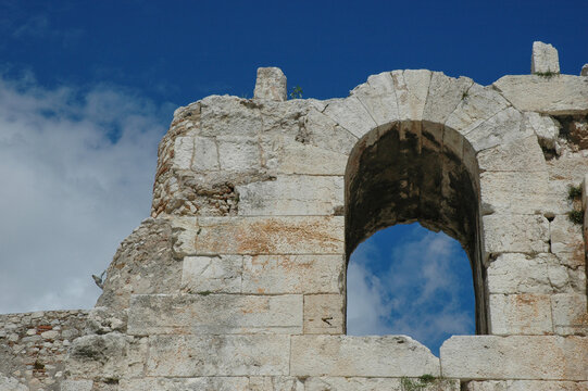 A detailed view of an ancient stone arch on the weathered facade of the Odeon of Herodes Atticus under a blue sky in Athens Greece.