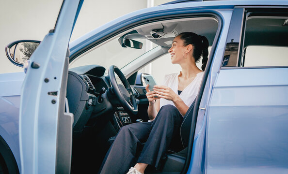 Young hispanic woman sitting in a car driver seat and using a smartphone application for parking payment or city map navigation