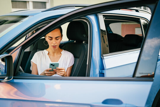 Young hispanic woman sitting in a car driver seat and using a smartphone application for parking payment or city map navigation