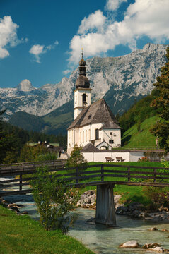 Iconic scenery of Ramsau in the Alps in Berchtesgaden, Bavaria, Germany. Mountains, tress, blue sky and a river frame the white church.