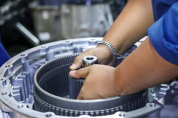 Close up view of a technician's hands assembling a large automatic gearbox component and planetary ring gear inside the casing at a repair workshop. © Jumain