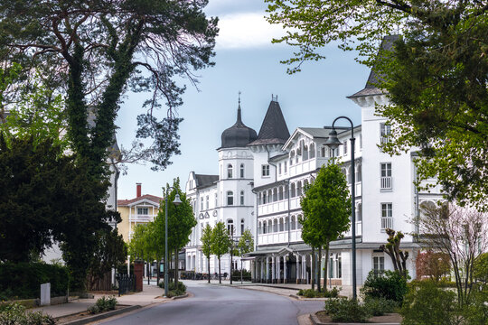 View of the classic white resort architecture and beautiful historic buildings along a tree-lined street in the coastal town of Sellin, Ruegen, Germany.