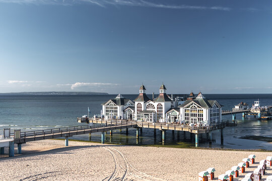 Beautiful view of the historic white Seebrucke Sellin pier building over the water, seen from the sandy beach lined with traditional beach chairs on R&uuml;gen, Germany.
