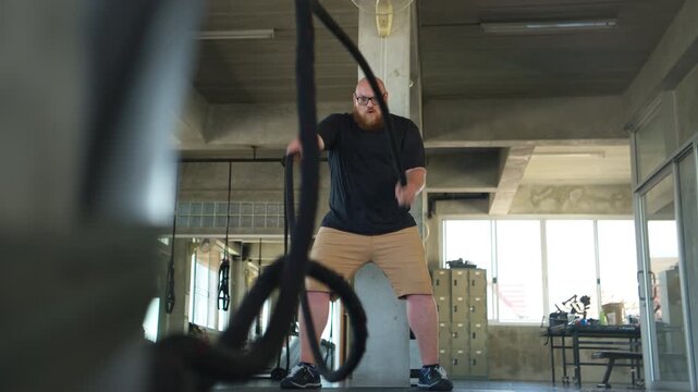 Overweight man performing battle rope training to improve fitness and build strength in a gym