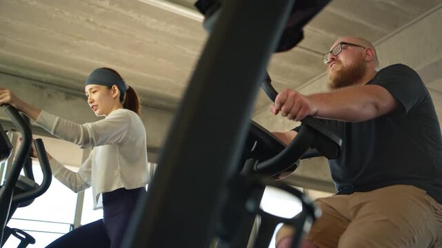 Female fitness trainer coaching an overweight beginner on elliptical machines during a cardio workout in a modern gym
