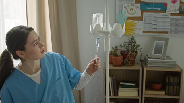 Young female nurse adjusting IV drip and sitting down to talk with senior patients in retirement home. Footage for senior care and geriatric healthcare commercials