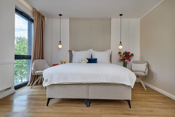 Sypialnia w nowoczesnym apartamencie z dużym  łóżkiem, fotelami, kwiatami i beżową szafą © arteffect.pl