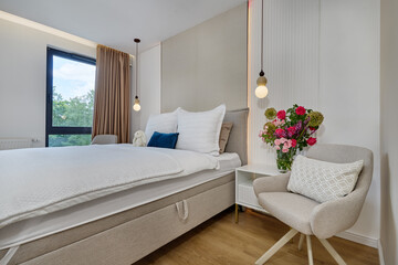Sypialnia w nowoczesnym apartamencie z dużym  łóżkiem, fotelami, kwiatami i beżową szafą © arteffect.pl