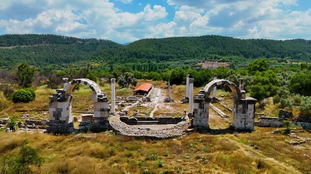 Cinematic aerial drone right pan over ancient Stratonikeia ruins with bouleuterion apse, Roman arches and Corinthian columns, Aegean pine mountains, Yatagan Mugla Turkey