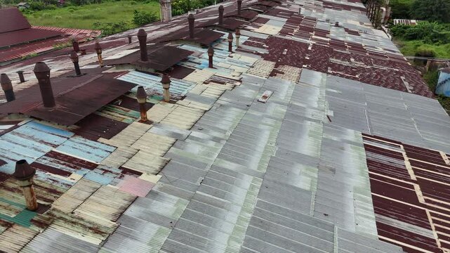 A rusted corrugated metal factory roof with a chimney vent and weathered, patchwork panels atop an industrial building.