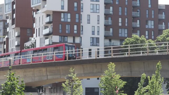 DLR trains crossing elevated railway bridge in Southeast London with modern residential apartments, sunny day, editorial