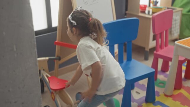 Girl holding a hobbyhorse and playing by a striped circus tent, abacus, dolls and train tracks scattered on a foam mat in a playroom; playful imagination.