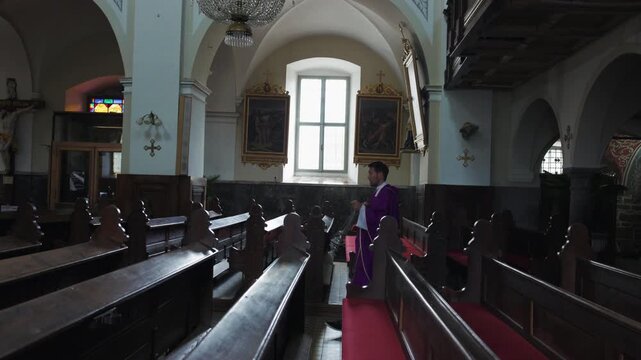 Catholic priest carrying and swinging a thurible of incense while walking through the aisle, in the empty church.