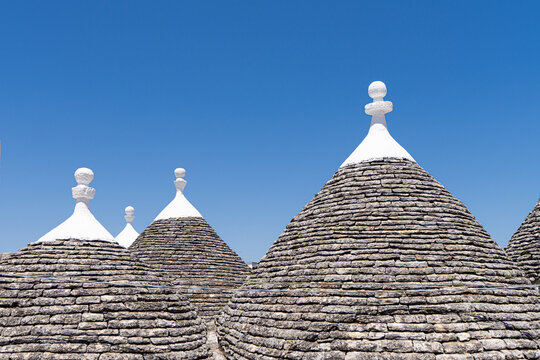 Traditional trullo stone rooftops with pinnacoli against blue sky in Alberobello, Italy