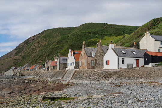 Aberdeenshire Crovie Fishing Village houses line the rugged Scottish coast beneath a large green hill and cloudy sky