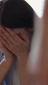 Vertical video Young woman sitting on sofa, looks pessimistic and sad, almost crying, man calming her down, softly touches and hugs her. Partnership and support concept.