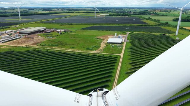 Aerial view of Chelveston Hybrid Solar and Wind Energy Farm with rows of solar panels and wind turbines in Wellingborough, England, United Kingdom.