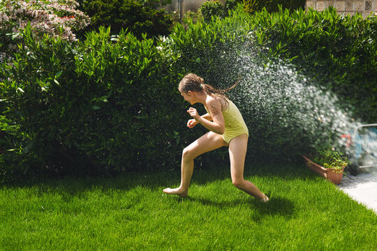 A cheerful child plays with water sprinklers in the garden during the summer. Creatively watering the garden&mdash;with fun and high spirits. An authentic, real little girl.