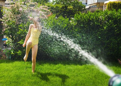 A cheerful child plays with water sprinklers in the garden during the summer. Creatively watering the garden&mdash;with fun and high spirits. An authentic, real little girl.