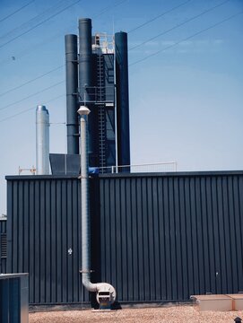Industrial rooftop ventilation stacks and exhaust pipes against clear blue sky with corrugated facade