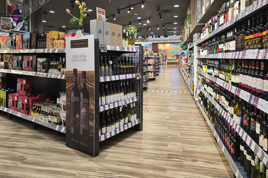 Penang, Malaysia - June 25, 2026: An eye-level view of a supermarket alcohol aisle featuring a Wakefield wine promotional display stand and long shelves stocked with various wine bottles.