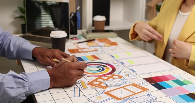 Creative team collaborating on UX and UI design using wireframes, interface components, color palettes, and planning materials to develop digital products through design thinking and teamwork.