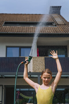 A cheerful child plays with water sprinklers in the garden during the summer. Creatively watering the garden&mdash;with fun and high spirits. An authentic, real little girl.