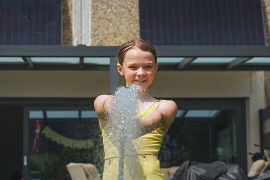 A cheerful child plays with water sprinklers in the garden during the summer. Creatively watering the garden&mdash;with fun and high spirits. An authentic, real little girl.
